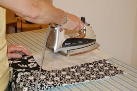 Pressing a pieced quilt top flat with an iron on an ironing board.