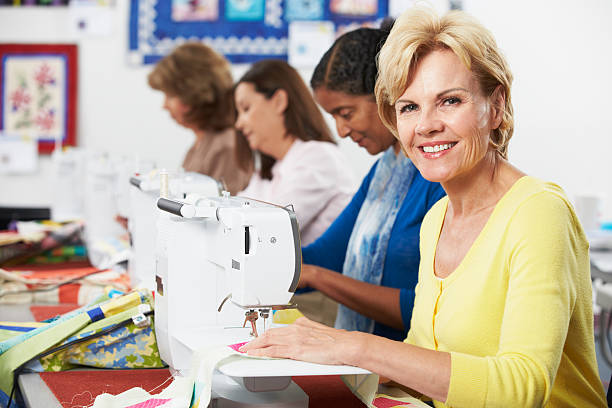 Group Of Women Using Electric Sewing Machines In class Smiling At Camera