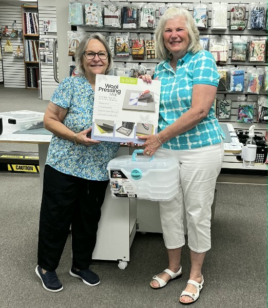 Barbara O’Brien, July 2026 drawing winner, at right, with owner Gloria Perkins at Glory Bee’s Sewing Center, holding an easy Wool Pressing Mat and a carrying case