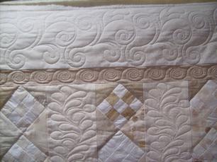 Close-up of a finished quilt showing feather and swirl longarm stitching.